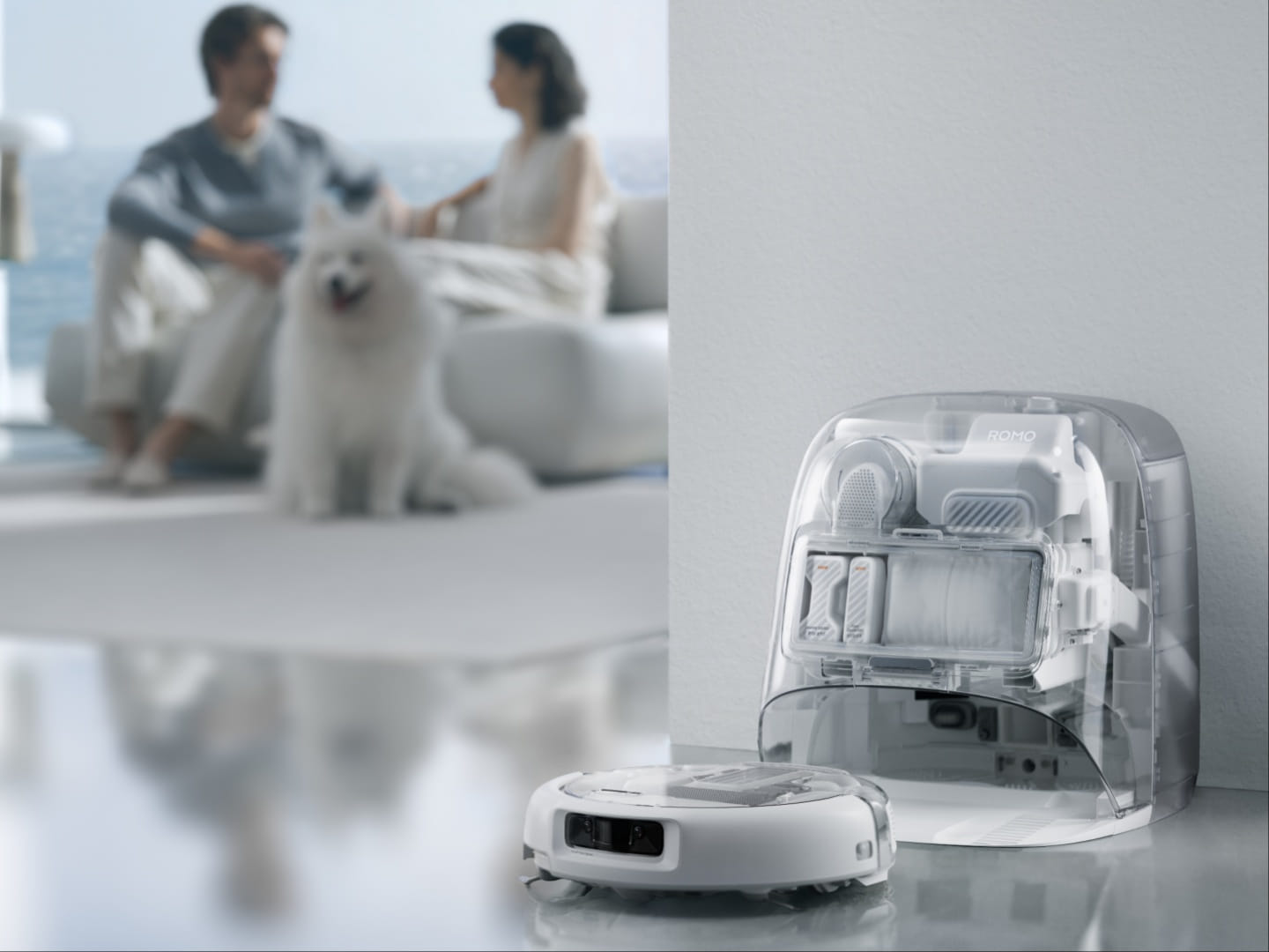 DJI Romo 2 com base translúcida ao lado de um casal e um cachorro em uma sala com vista para o mar