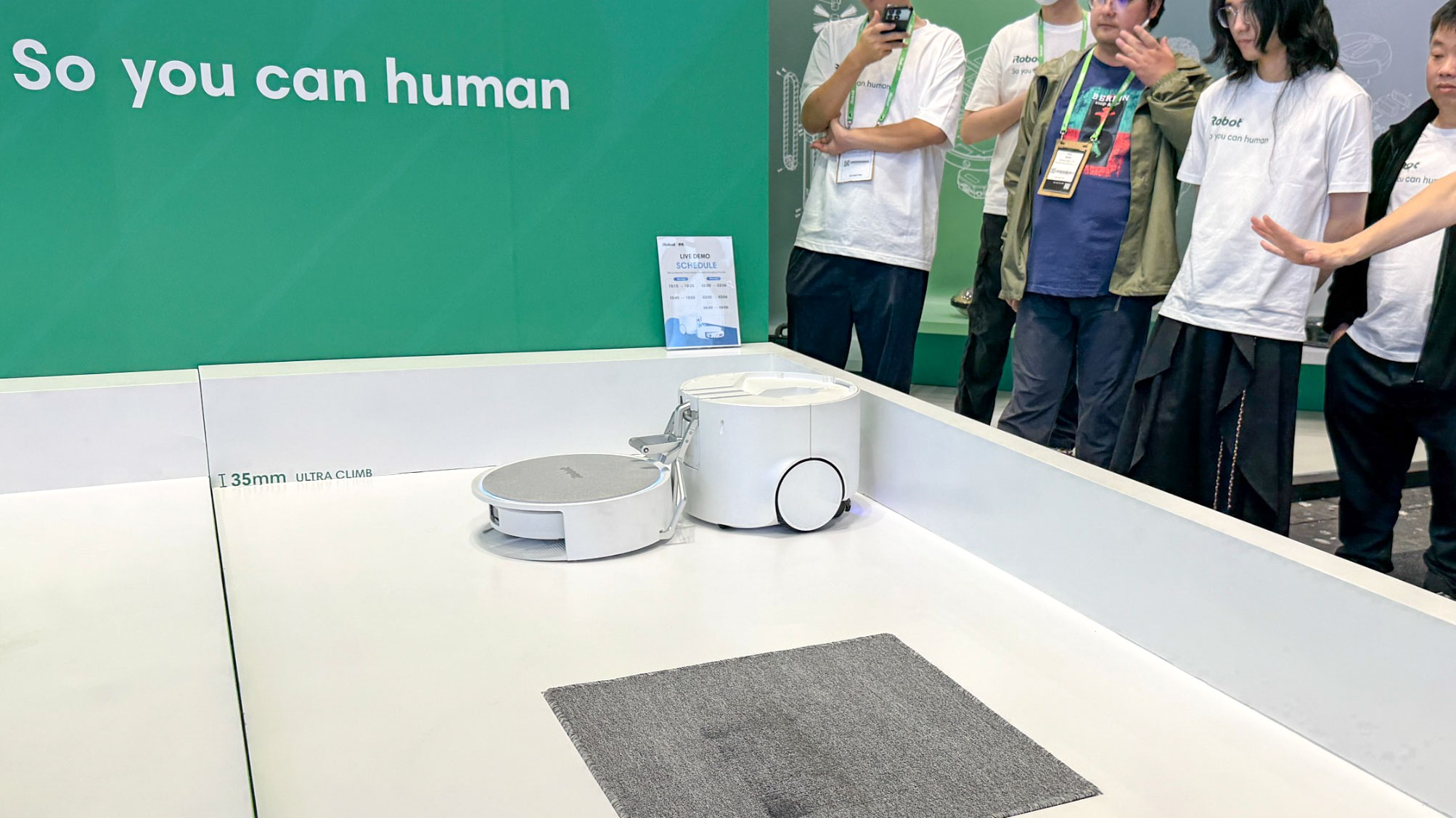 Demonstração do Roomba Duo no estande da iRobot na IFA 2026, com o robô companheiro sendo solto pelo braço sobre uma pista com degrau de 35 mm