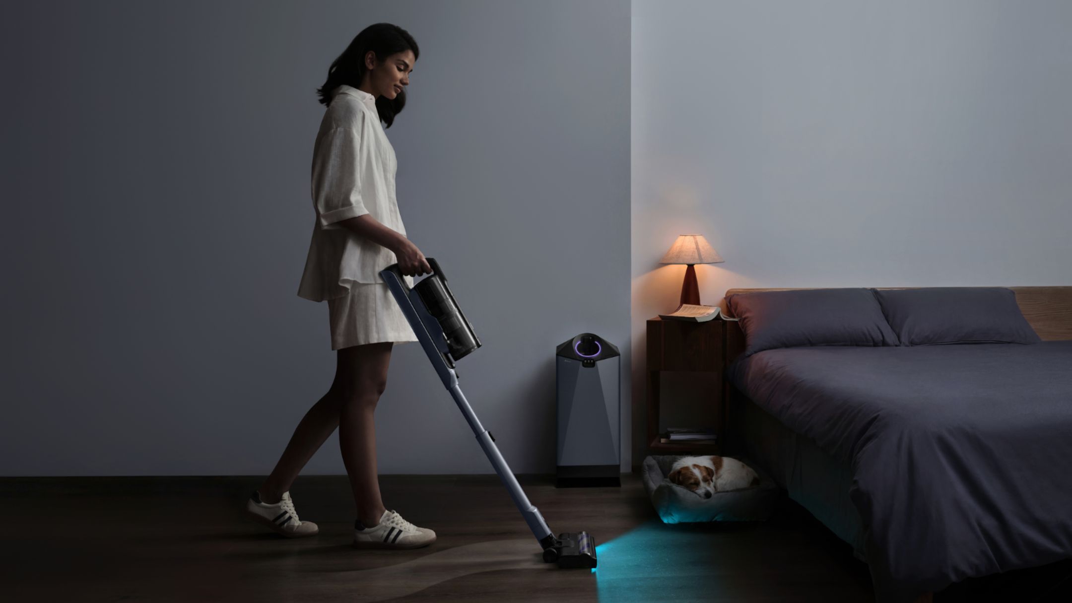Aspirador vertical sem fio Narwal V50 Cube em uso num quarto, com a base de autoesvaziamento ao lado da cama