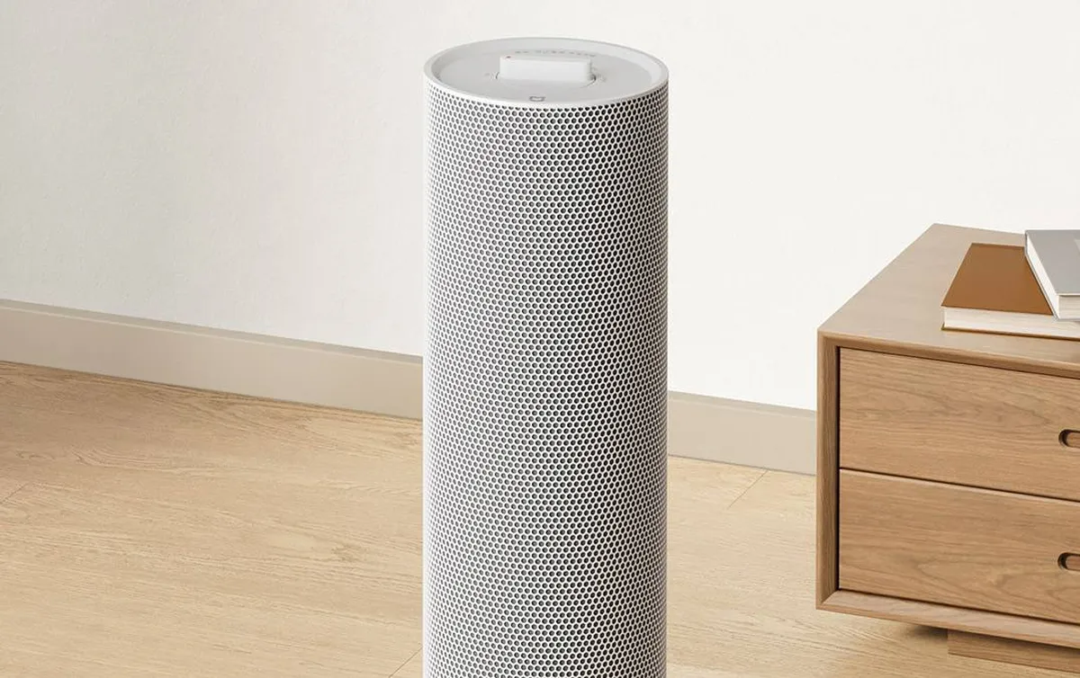 Aquecedor de torre Xiaomi Mijia com corpo cilíndrico microperfurado, instalado ao lado de um móvel de madeira