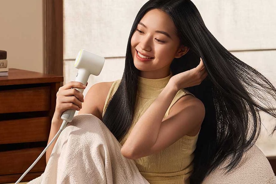 Mulher sentada secando o cabelo comprido com o Mijia Mini na cor bege